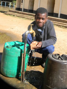 Norton,Zimbabwe,7July 2017.A  kneeling  young  African  kid  drinking  water   from  a  tap  using  his  hands. 					 clipart