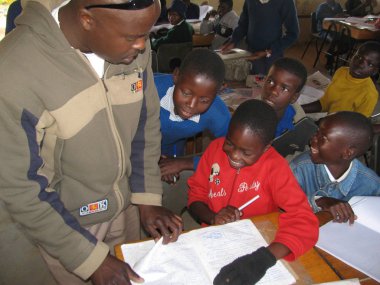Norton, Zimbabwe, 29september 2014. Diğer çocuklar bir sınıf üzerinde görünüyor iken bir çocuğun kitap işaretleme bir ilkokul öğretmeni. Zimbabwe bir çok yüksek okuma-yazma oranı olan.                               