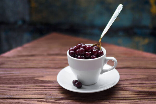 Сладкие вишни в белой чашке и чайная ложка на деревянном столе, выбранный фокус, вид сбоку
