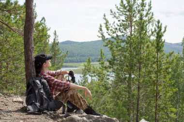 yere packback ve dürbün ile ağaçları arasında Hill'de oturan uzun yürüyüşe çıkan kimse yan görünüm.