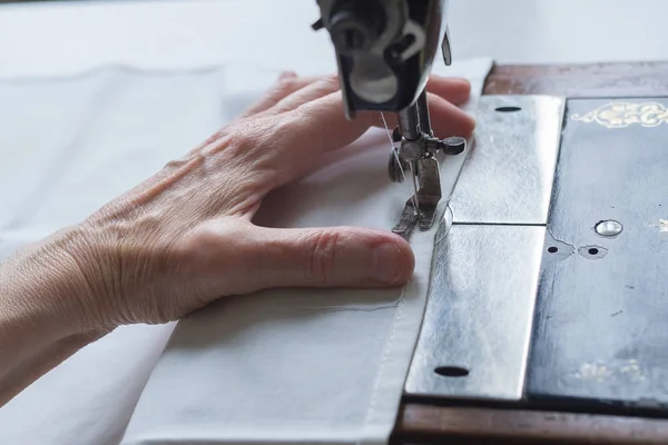 Процесс шитья. Нога старинной винтажной швейной машинки и руки пожилой женщины. Селективный фокус — стоковое фото