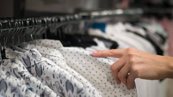 Rack with hangers in a store. Female hand holds some shirt and choose some item. Selected focus.