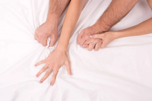 Hands of couple who making love in bed on white crumpled sheet, focus on hands