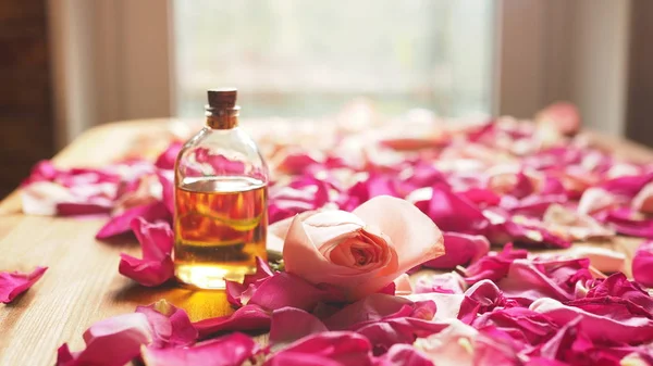 Flesje aroma olie met bloemblaadjes van rozen op de houten ondergrond, geselecteerde focus — Stockfoto
