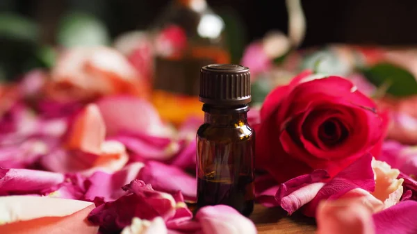 Glass bottle of aroma oil among roses petals on the table, natural raw material, selected focus