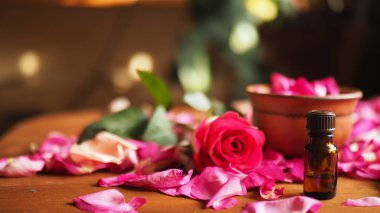 Kil kase ve aroma yağı karanlık cam şişe üzerinde ahşap masa, doğal hammaddeler, gül yaprakları arasında odak seçili