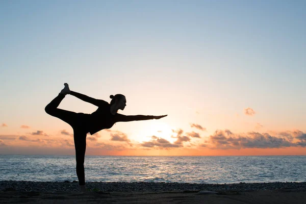 Gün batımında sahilde yoga yapan bir kadın silueti.