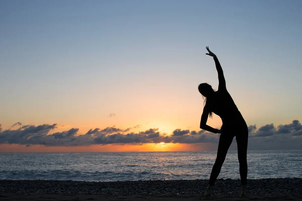 Silueta humana haciendo ejercicio matutino en la playa al amanecer — Foto de Stock