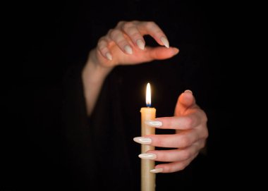 Candle and female witch hands with sharp pearl nails. Divination and witchcraft, low key.