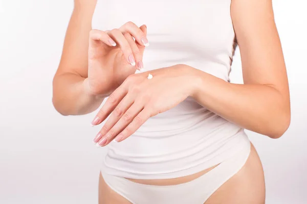 Mãos femininas com manicure francês aplicando creme de mão, fundo branco, close-up, vista frontal — Fotografia de Stock