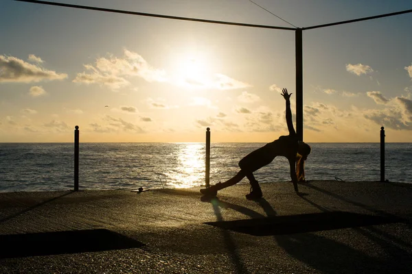 Silhouette of woman doing yoga on the dock by the sea at sunrise