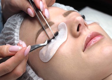 Kirpik uzatma yordamı. Kadın yüz ve uzmanlar parmak cımbızla, seçici odak, yakın