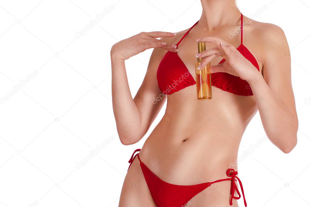 Female sexy tanned fit body in red classic bikini with oil spray bottle, isolated on white