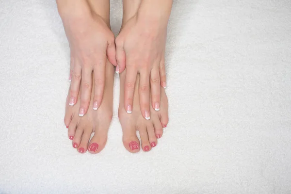 Female feet on white terry towel and hands. Woman touches her skin, close up. French manicure and pink pedicure. — Stock Photo, Image