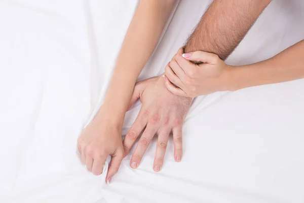 Hands of couple who having sex in bed on white crumpled sheet, focus on hands