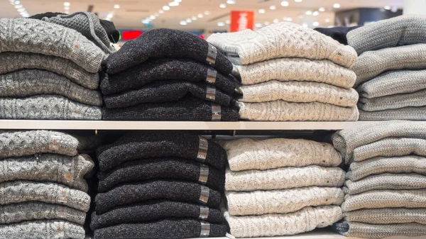 Rack of clothes in a store. Piles of warm sweaters different sizes, close up