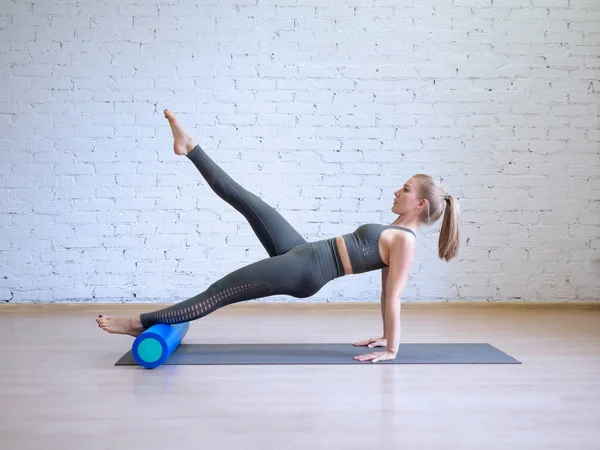 Gri spor takım elbiseli beyaz genç kadın fitness silindiri, loft tarzı arka plan, tonda açık mavi ile matematik pilates egzersiz yapıyor