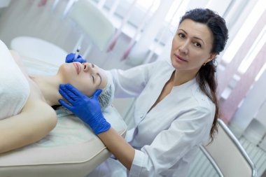 Kozmetolojist, elinde hasta ve tek kullanımlık şırınga ile tek tip kıyafetli güzellik salonunda çalışıyor. Müşteri kapalı gözleri ile bir kanepede yatıyor ve prosedür için hazır.