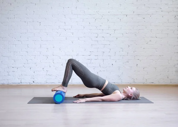 Köpük silindir üzerinde gluteal köprü. Fitness stüdyosunda özel ekipmanlarla pilates yapan genç beyaz kadın.