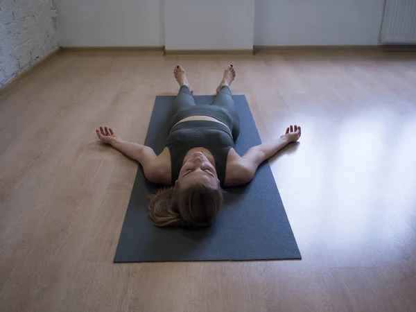 The shavasana. Woman laying on mat in relaxing pose on the floor, yoga class, front view