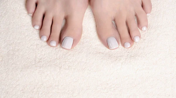 Female toes with white pedicure on ivory terry towel, close up. Woman bare feet.