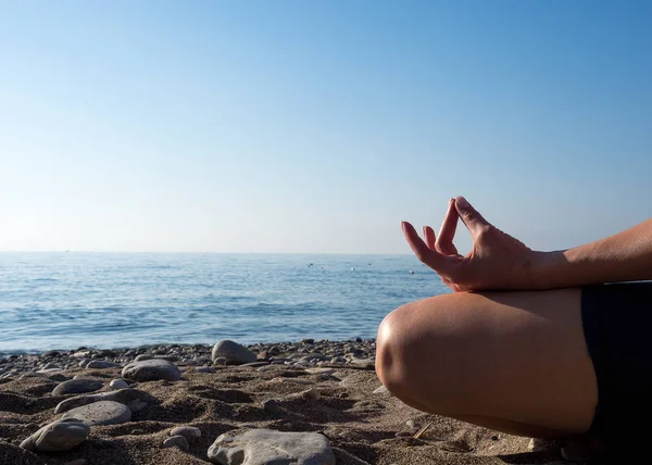 Meditatif devlet. Deniz in yanında kumda oturan ve parmaklarını katlayarak işaret eden kişi, güneşli gün, seçici odak.