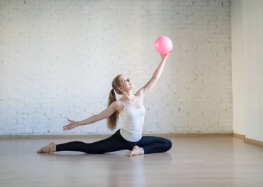 Genç beyaz kadın küçük pembe fit topu ile pilates pratik, fitness stüdyosunda çekici poz, loft tarzı, seçici odak.