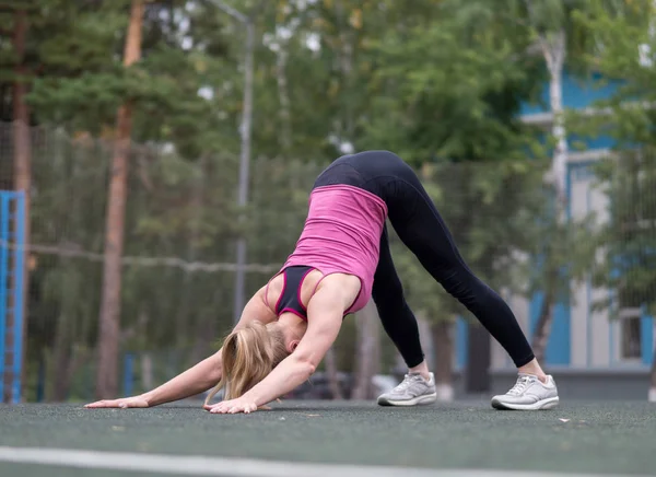 Fit καυκάσιο κορίτσι κάνει γιόγκα στο αθλητικό έδαφος εξωτερική, επιλεκτική εστίαση. Φάτσα σκύλου κάτω πόζα — Φωτογραφία Αρχείου