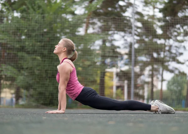 Fit blond atrakcyjna dziewczyna robi ćwiczenia w górę psa na boisko sportowe na zewnątrz, selektywne skupienie — Zdjęcie stockowe