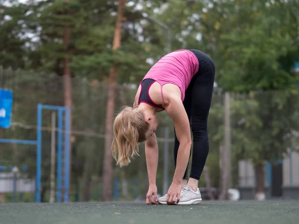 Blond kaukaski dziewczyna robi rozgrzewkę przed treningiem na terenie sportowym na zewnątrz, selektywne skupienie. — Zdjęcie stockowe