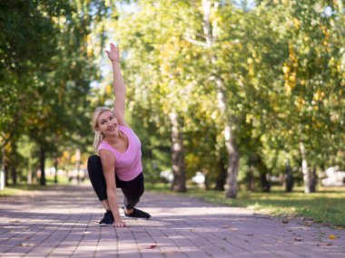 Beyaz tebessümlü orta yaşlı atletik kadın şehir parkında dışarıda çalışıyor.
