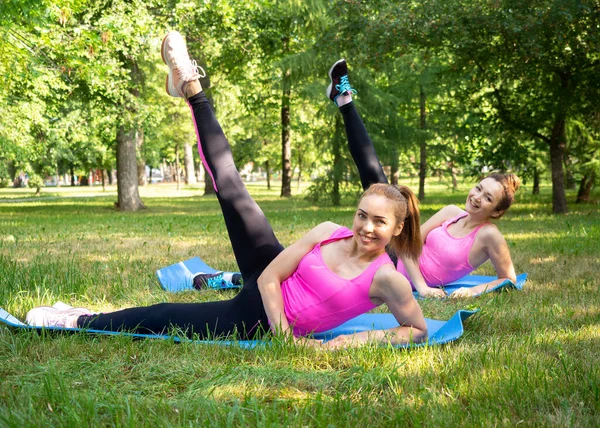 Две кавказские улыбающиеся девушки занимаются спортом в общественном парке летом на свежем воздухе, избирательный фокус — стоковое фото