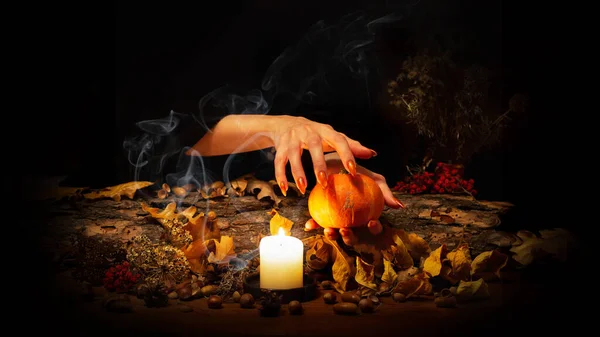 森の魔女は火のろうそくと暗闇の中で祭壇の上のカボチャを通過します。ナッツの間で長い鋭い爪を持つ女性の手,魔法のハーブ,乾燥葉,アコーン,選択した焦点,低キー — ストック写真