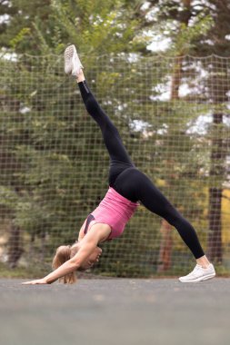 Kafkasyalı fit kadın bir bacağı yukarıda köpek egzersizi yapıyor. Yazın spor sahasında yoga, dikey fotoğraf, seçici odaklanma..