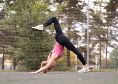 Çekici fit sarışın kadın köpek egzersizi yapıyor, bir bacağı yukarıda ve eğiliyor, ikiye bölünmüş olarak. Yazın spor sahasında yoga, seçici odaklanma..