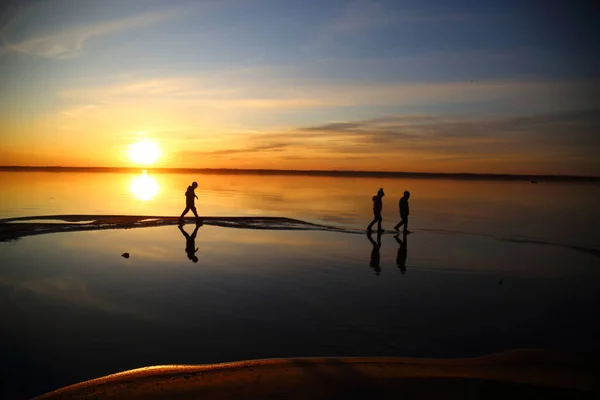 Beautiful sunset with silhouettes of children and reflection in — Stock Photo, Image