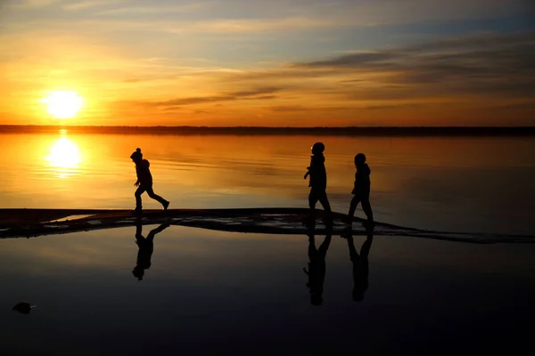 Hermosa puesta de sol con siluetas de niños y reflexión en —  Fotos de Stock