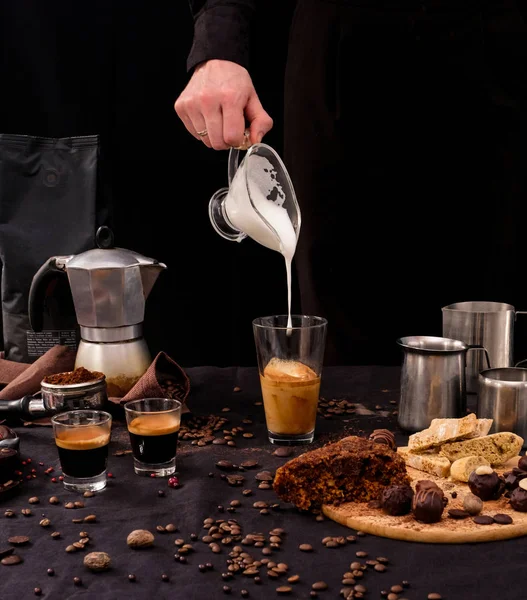 Barista brews coffee. Candy, pie, coffee on the table. Black background&