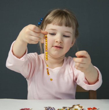 Boncuk iş parçacığı ve bilezik, gri arka plan yapma sevimli küçük kız