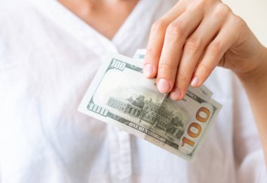 Woman's hand is holding two hundreds of dollars, neutral background clipart