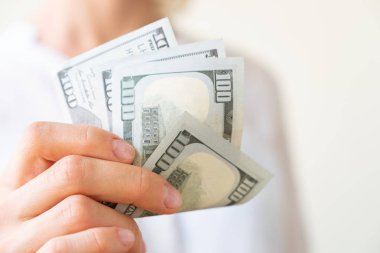 Woman's hand is holding two hundreds of dollars, neutral background clipart