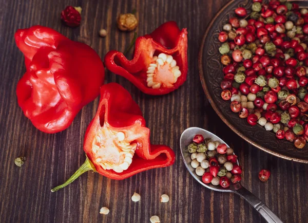 Fresh red peppers in the form of a roses, peas of pepper (red, white, green) on a wooden background