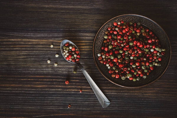 Peas of a red, green, white pepper in the spoon and in a copper saucer on a wooden background