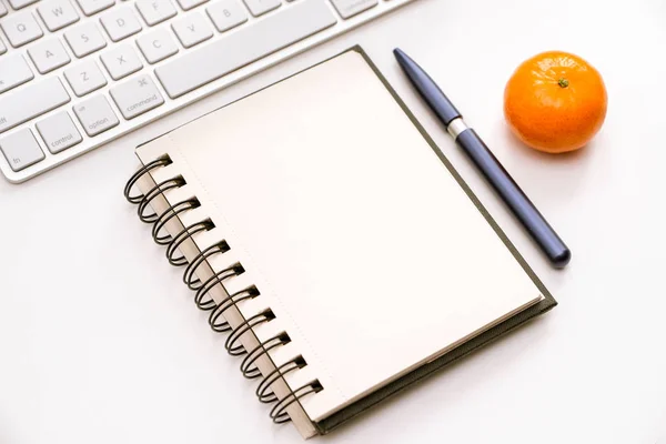 A fragment of the workplace with a keyboard and an opened notebook on a white desk