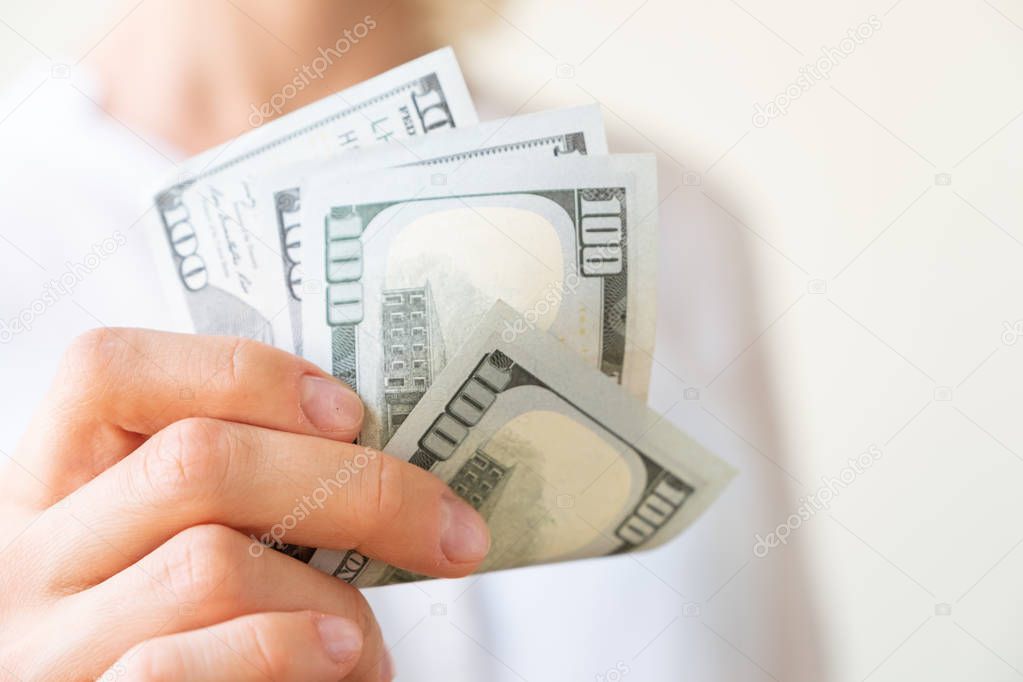 Woman's hand is holding two hundreds of dollars, neutral background