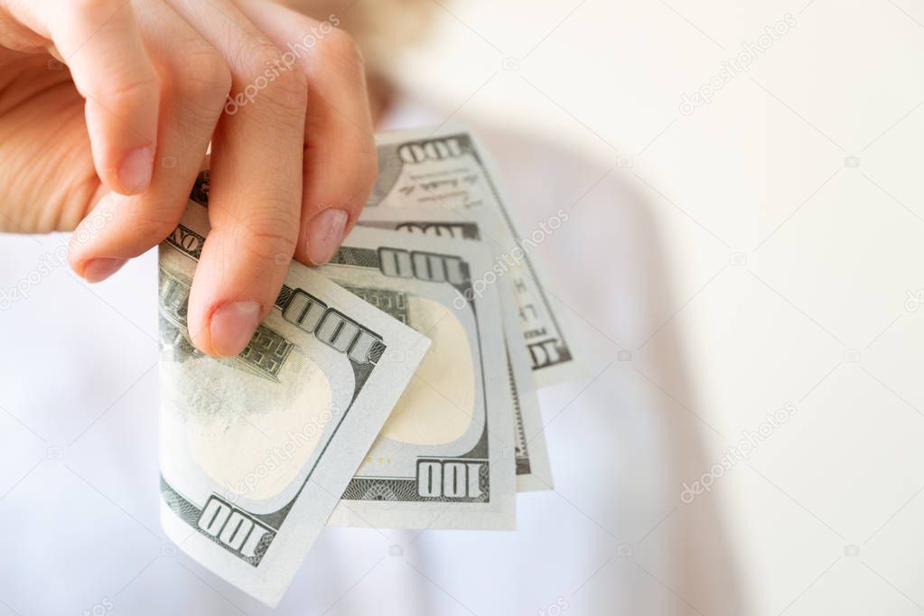 Woman's hand is holding two hundreds of dollars, neutral background