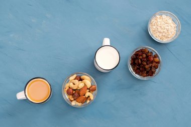 Çok kolay, hafif ve sağlıklı kahvaltı sağlıklı bir yaşam tarzı için: taze süt, portakal suyu, fındık, Kuru üzüm, yulaf gevreği. Mavi arka plan.