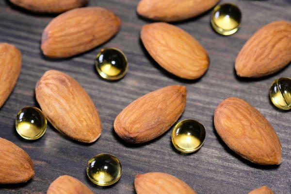 Almond and capsules with vitamin, wooden background