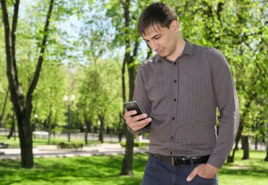 Yaz yeşil zemin üzerine bir cep telefonu tutan genç bir adam portresi