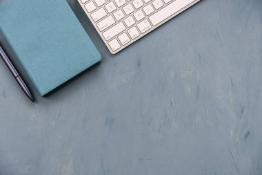 Bir klavye, mavi bir kalem ve defter üzerinde mavi masa üstü.